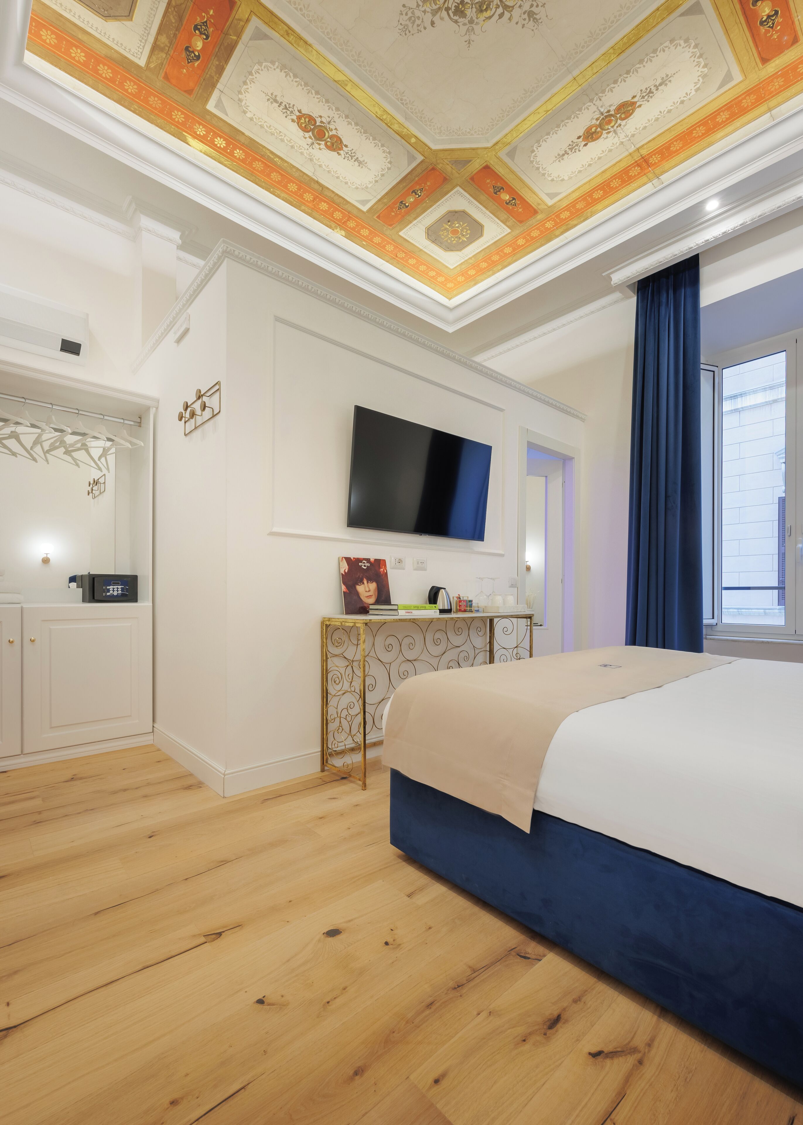 Ein Hotelzimmer mit einem großen Bett, einem an der Wand montierten Fernseher, einem Schreibtisch mit Computer und einem Kleiderschrank.