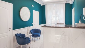 A modern bathroom with a large mirror, white vanity, and a blue chair. - SM Mellini Relais (Rome)