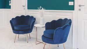 A room with teal walls, a large marble clock, two blue velvet armchairs, a small white table, and a white door. - SM Mellini Relais (Rome)