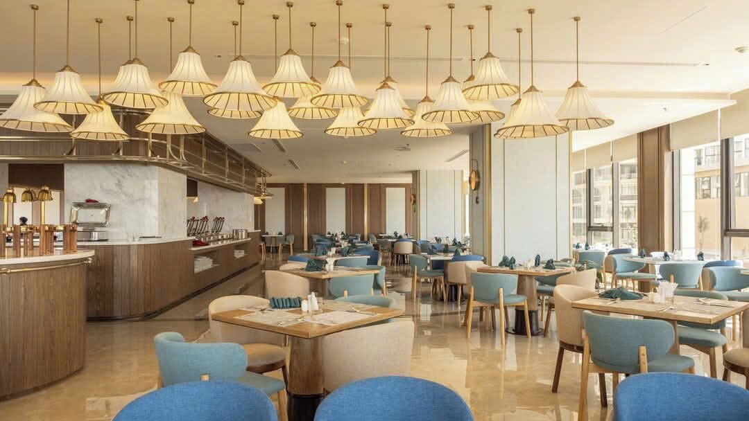 Un restaurant moderne doté de plusieurs tables et chaises, d’un bar et d’un éclairage suspendu.