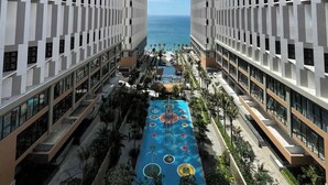 A high-rise hotel with a central pool, surrounded by balconies and a view of the ocean. - Apec Mandala Mui Ne - Sapphire Apartment (Mui Ne)