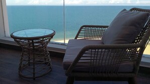 A wicker chair with a cushion and a glass table by a window overlooking the sea. - Apec Mandala Mui Ne - Sapphire Apartment (Mui Ne)