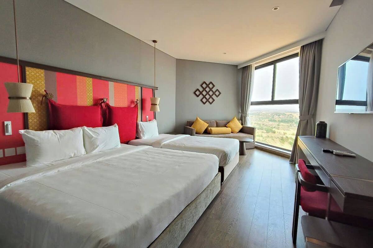 A hotel room with two beds, a desk, and a view of the outdoors.
