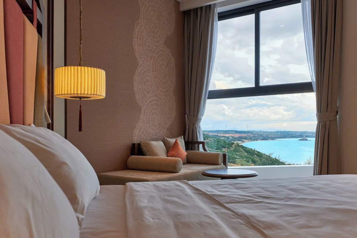 A hotel room with a large bed, a sofa, a small table, and a view of a body of water and landscape.