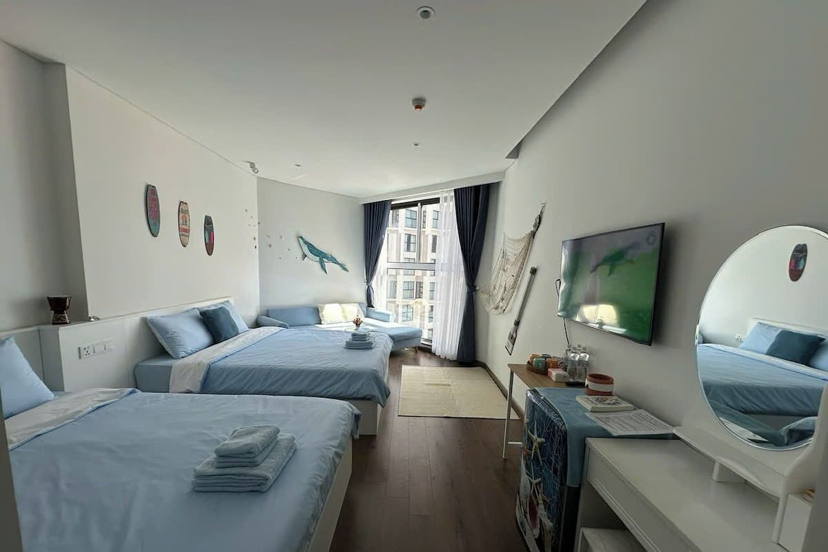 A modern hotel room with two beds, a desk, a TV, and a large window with curtains.