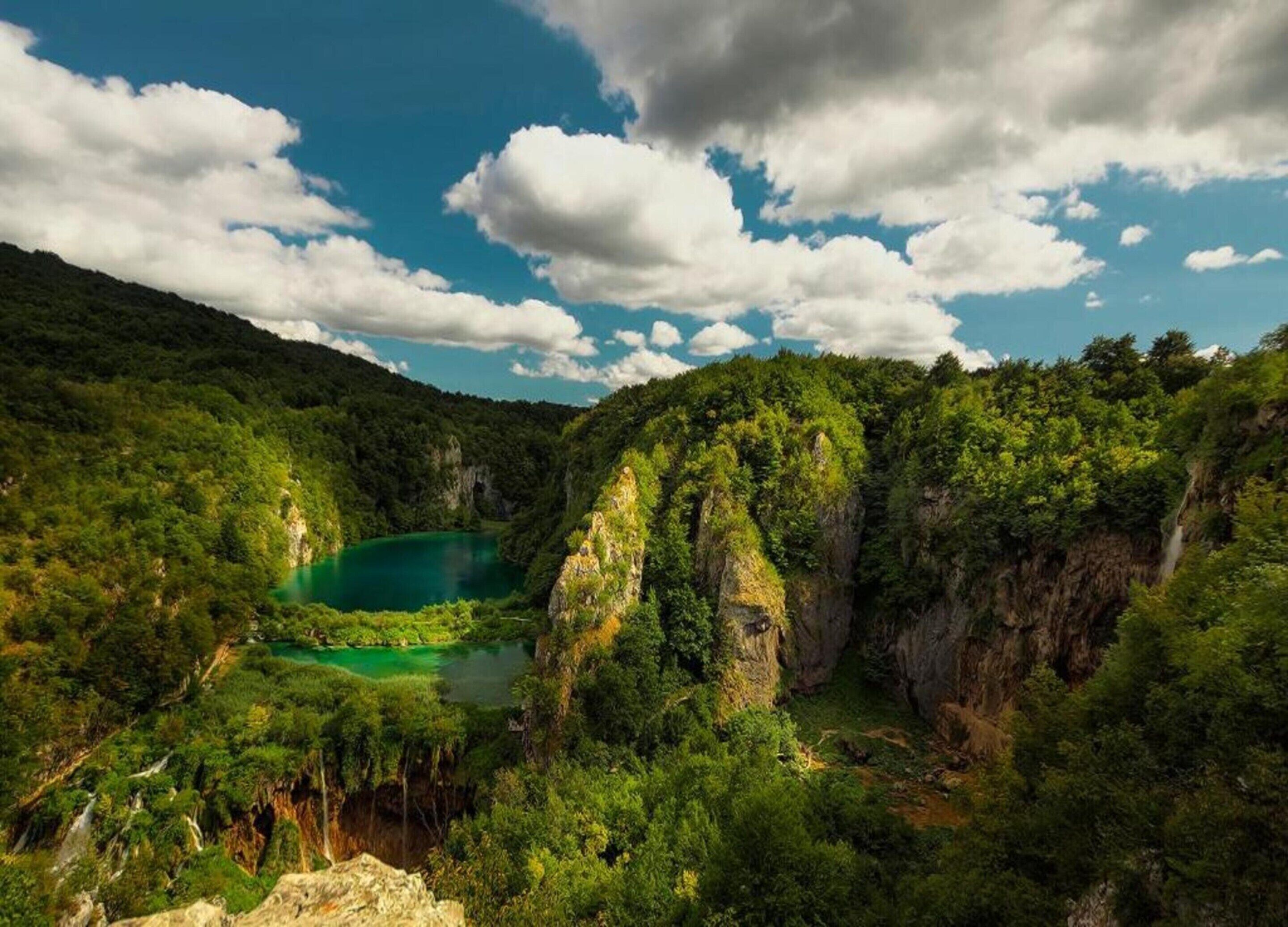 A mountainous landscape with a turquoise lake, dense forest, and rocky cliffs.
