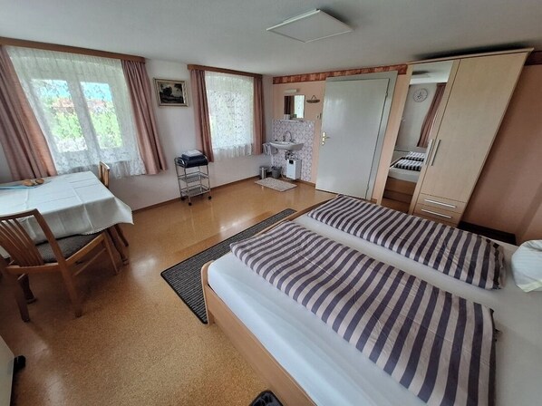 A hotel room with two beds, a desk, a chair, a small sink, and a wardrobe.