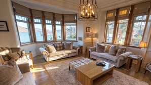 A cozy living room with a large window overlooking a lake, furnished with sofas and a coffee table. - Stronachlachar Lodge - spacious with cinematic views, direct access to loch. (Stirling)
