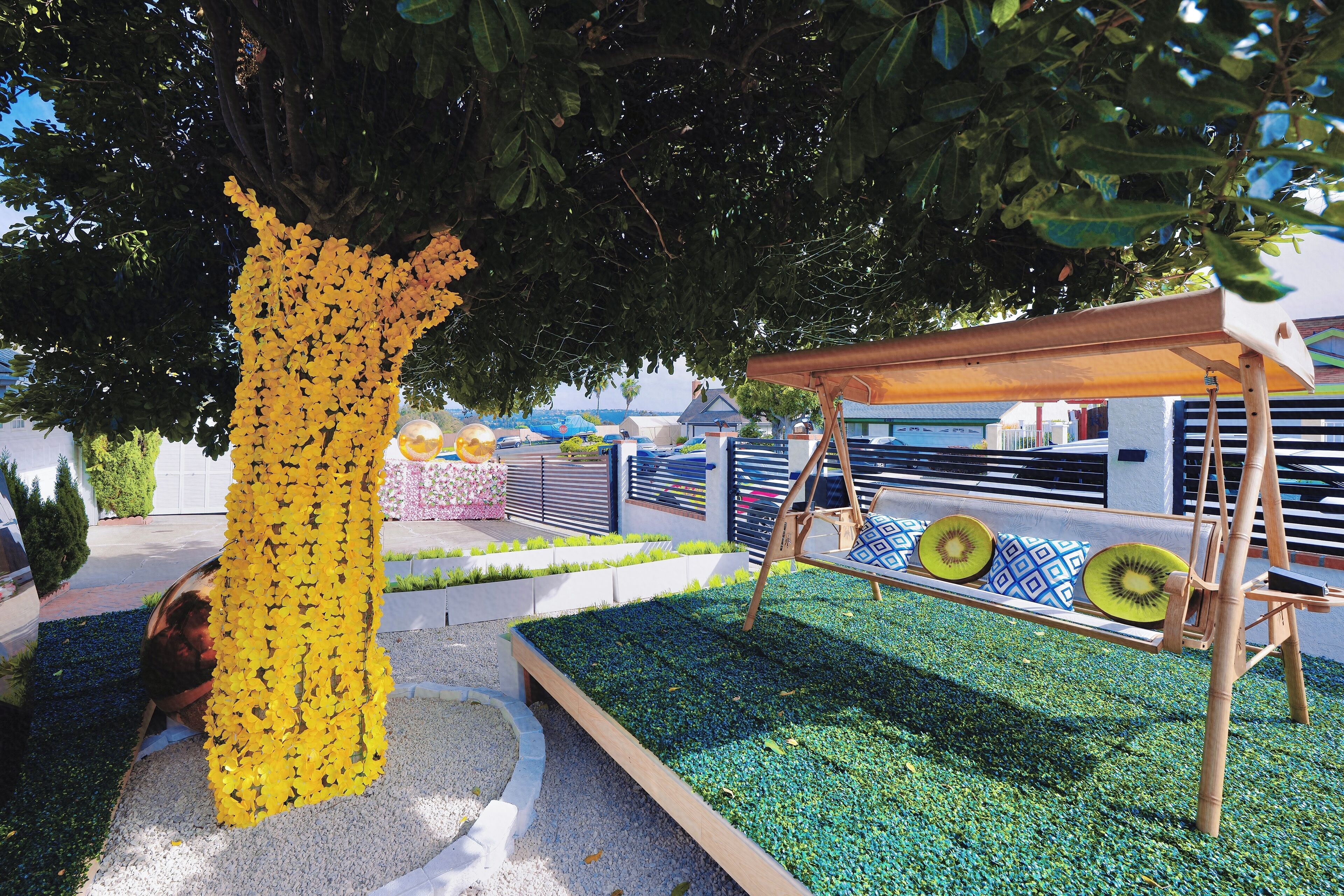 A garden area with a swing set, a tree with yellow flowers, and a bench with patterned cushions.