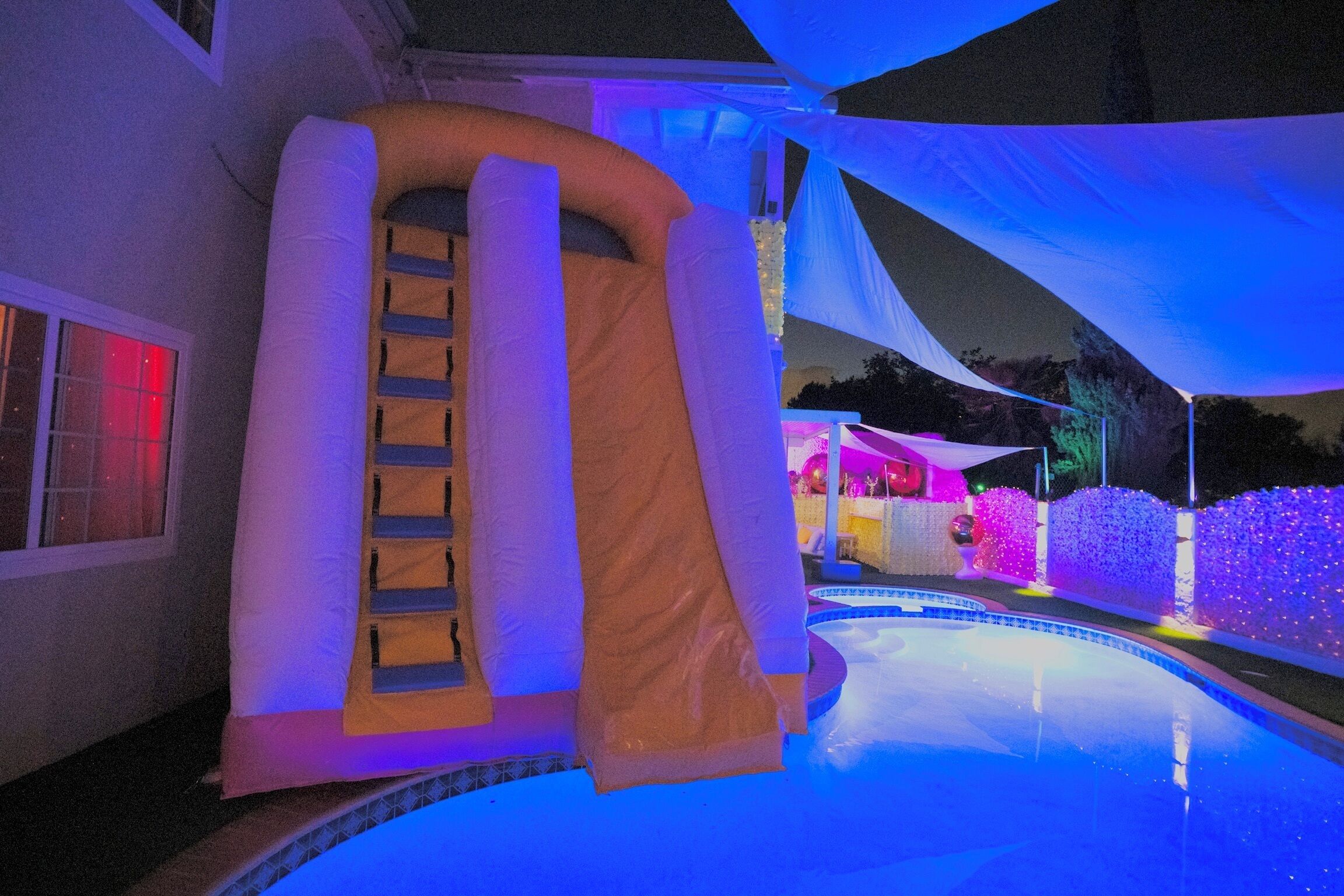 Una piscina con uno scivolo, circondata da un tendone bianco e illuminata da luci colorate.