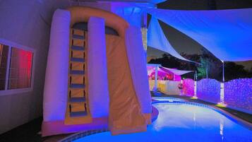 Una piscina con uno scivolo, circondata da un tendone bianco e illuminata da luci colorate.