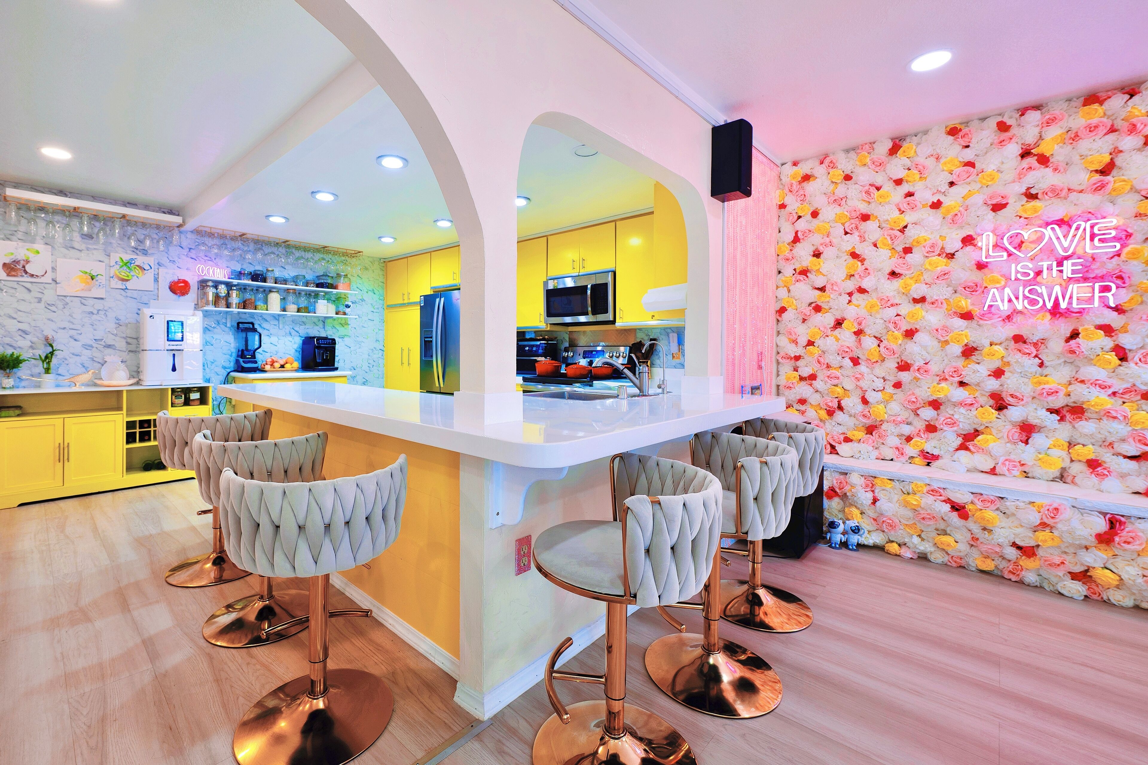 A modern kitchen with yellow cabinets, a white countertop, and a bar area with four bar stools.