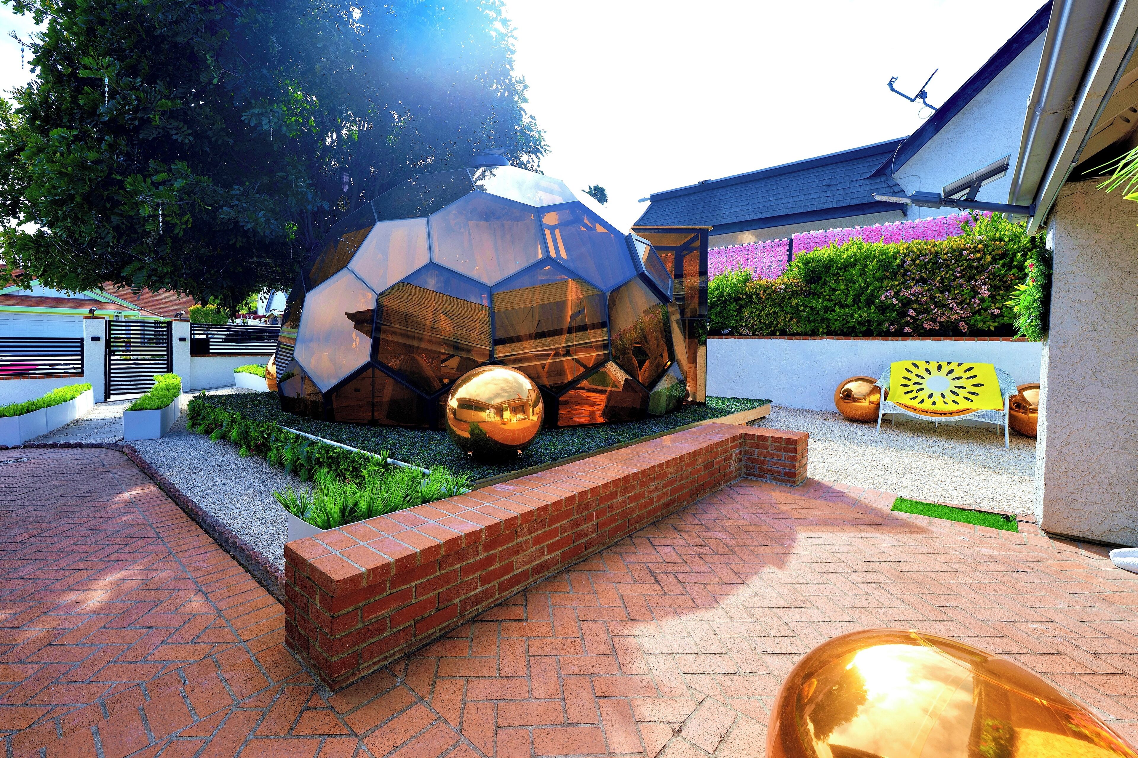 Un giardino con una scultura geometrica, un vialetto in mattoni e piante in vaso.