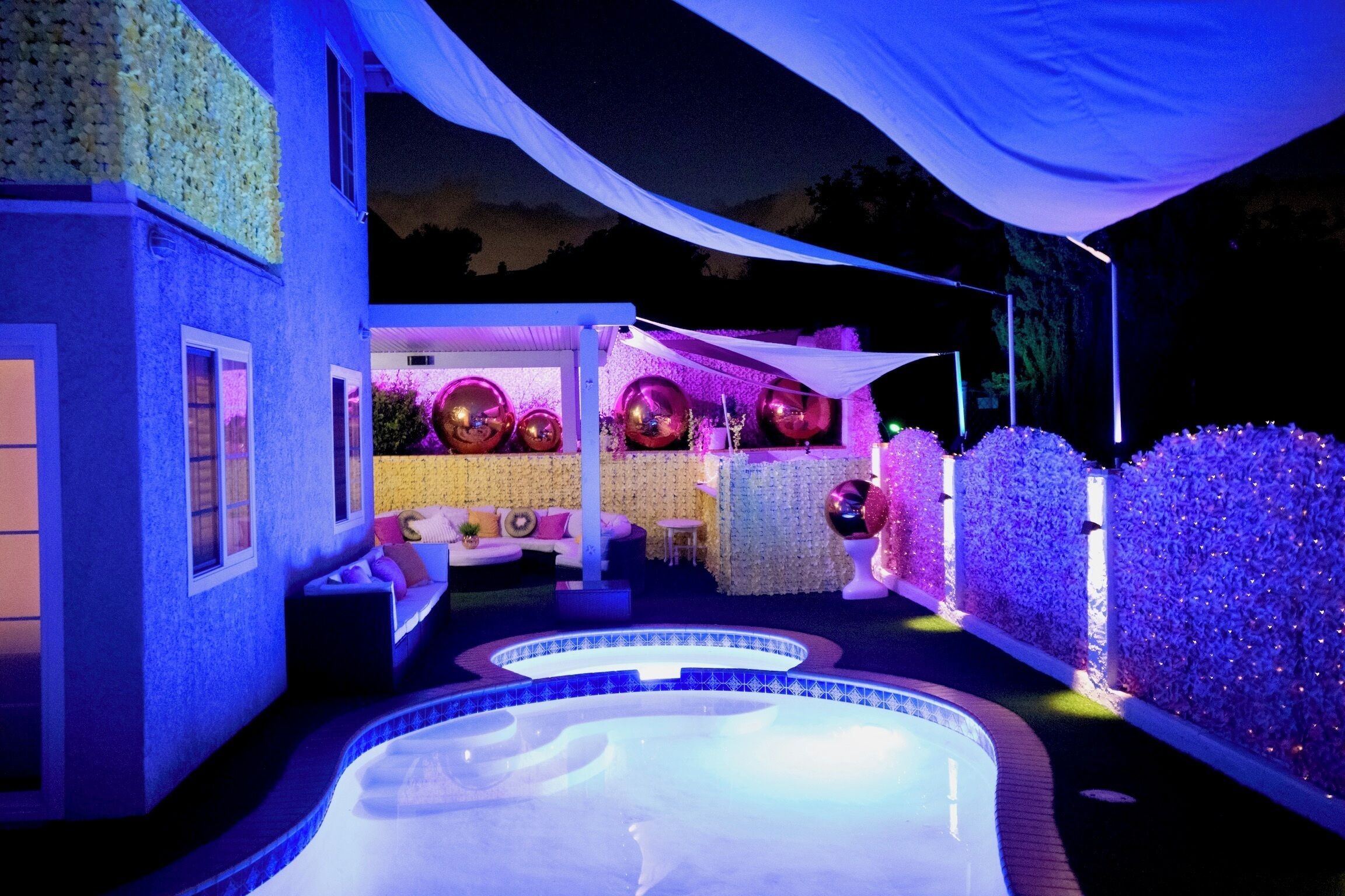 Area piscina con idromassaggio, zona relax coperta con cuscini e decorazioni come palloncini e una tenda bianca.