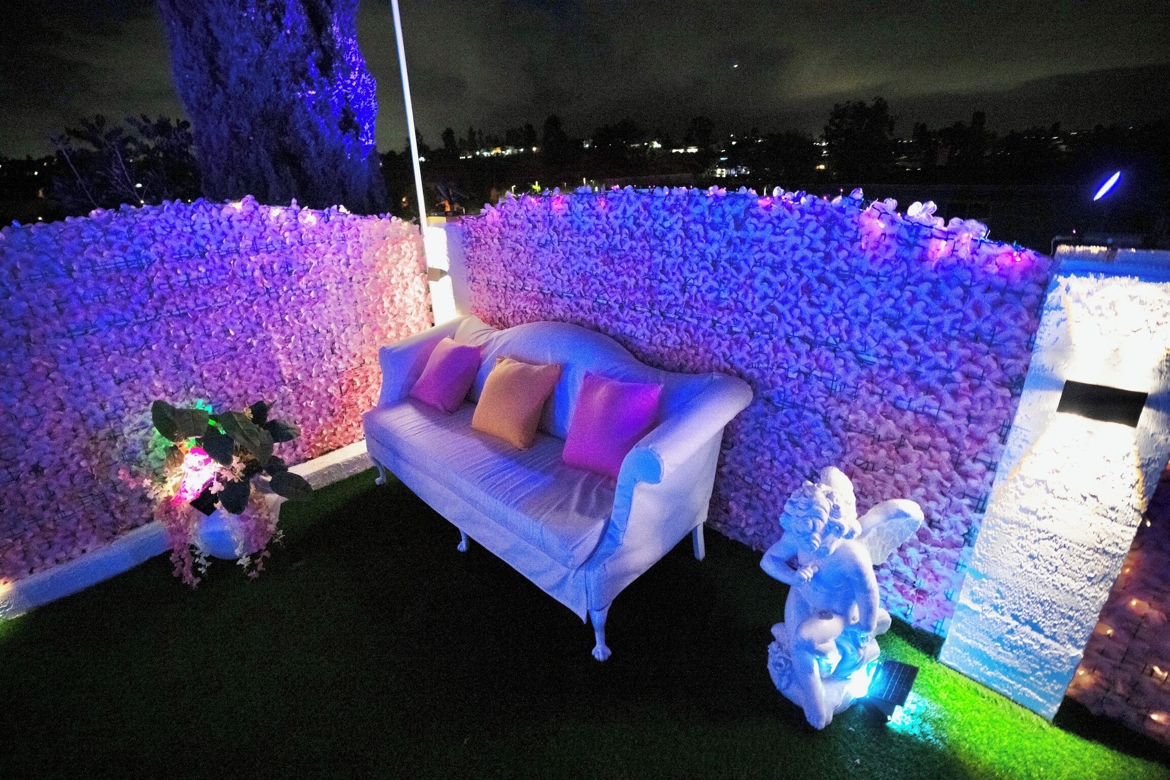A white sofa with cushions, a decorative wall of flowers, and a statue of an angel.