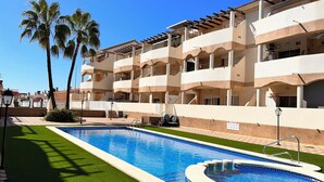 A hotel with a swimming pool, palm trees, and a two-story building with balconies. - Lovely Holiday Place with pool, A/C, TV, WIFI - Playa Sol Vinaros (VC)