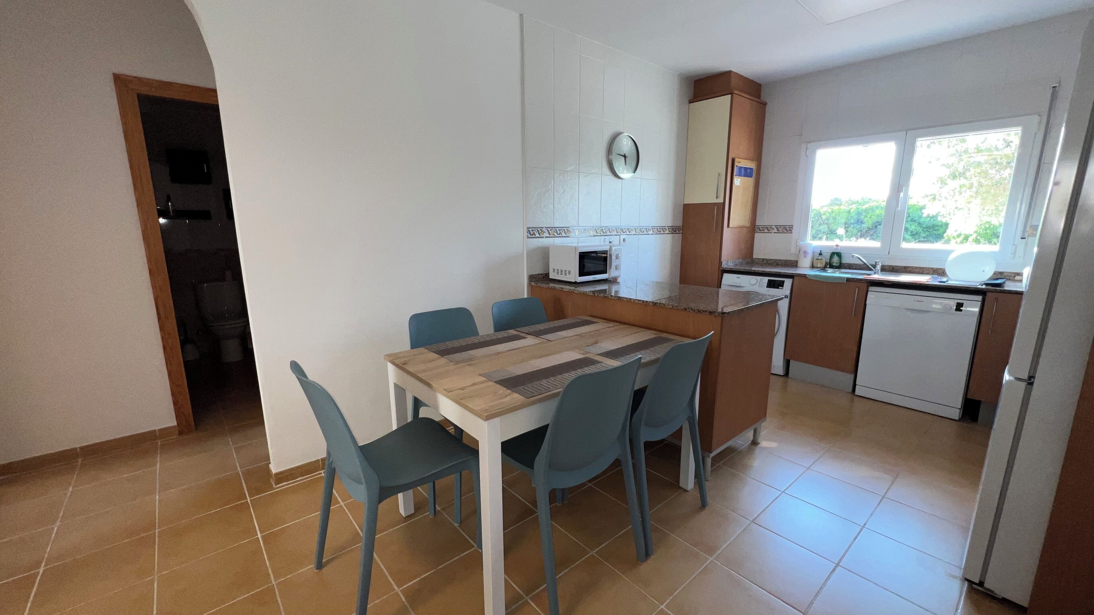 A compact kitchen with a dining table, chairs, a microwave, a sink, and a refrigerator.