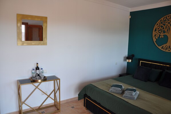 A bedroom with a bed, a bedside table with a tray of bottles, and a wall decoration. - Villa El Dorado B&B and Wellness (Competa)