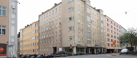 A multi-story building with a ground-floor commercial space, several parked cars, and a pedestrian crossing.