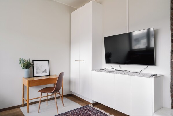 Une chambre moderne avec un bureau en bois, une chaise, un téléviseur fixé au mur et un tableau encadré accroché au mur.