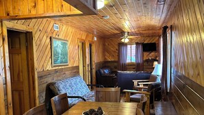 A wooden cabin interior with a dining table, chairs, a sofa, and a fireplace.