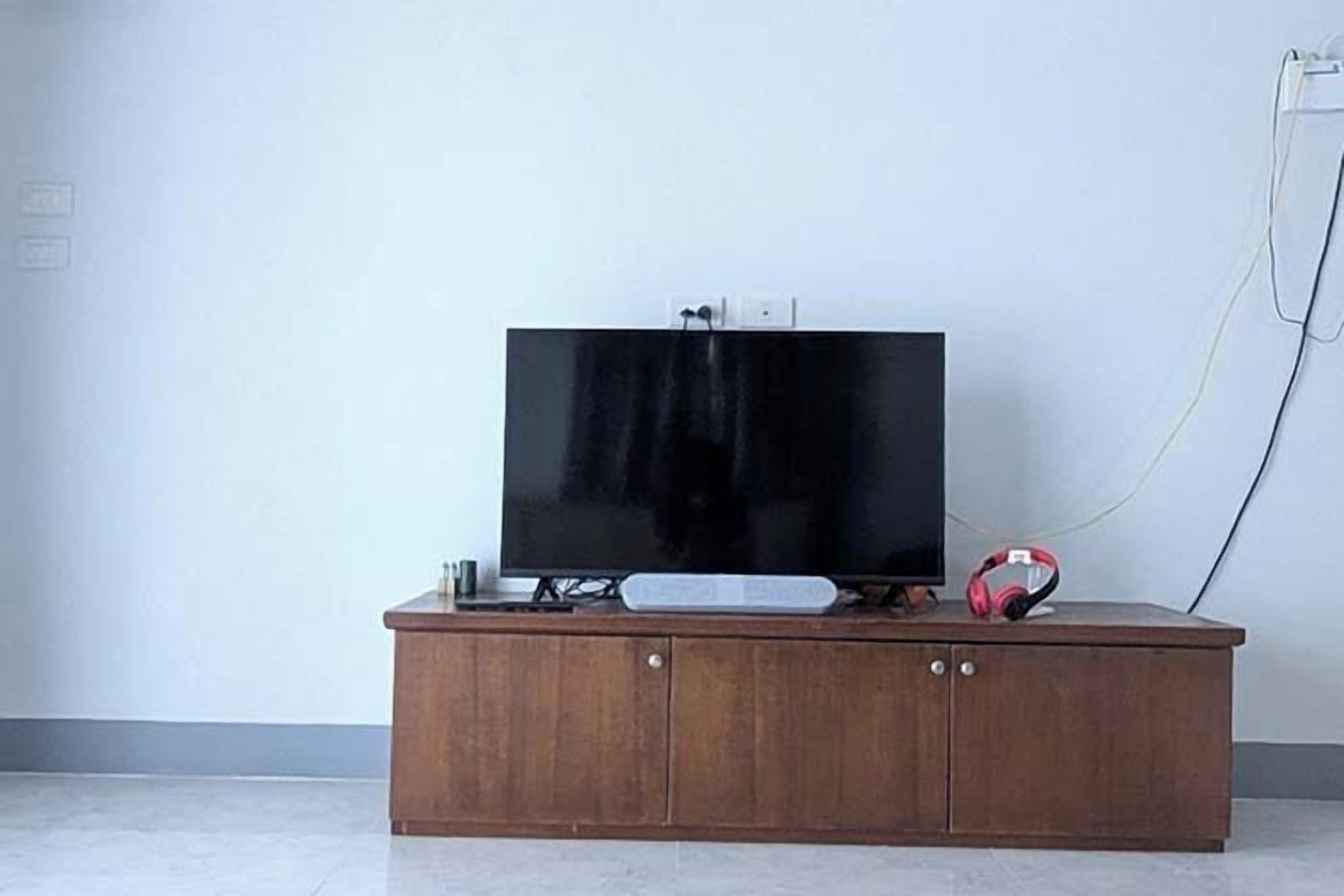A wooden TV stand with a flat-screen TV, a remote control, and a pair of headphones on top.