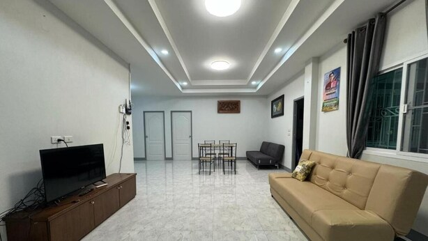 Una sala moderna con un televisor de pantalla plana sobre un mueble de madera, un sofá color beige, una mesa de comedor con sillas e iluminación empotrada en el techo.