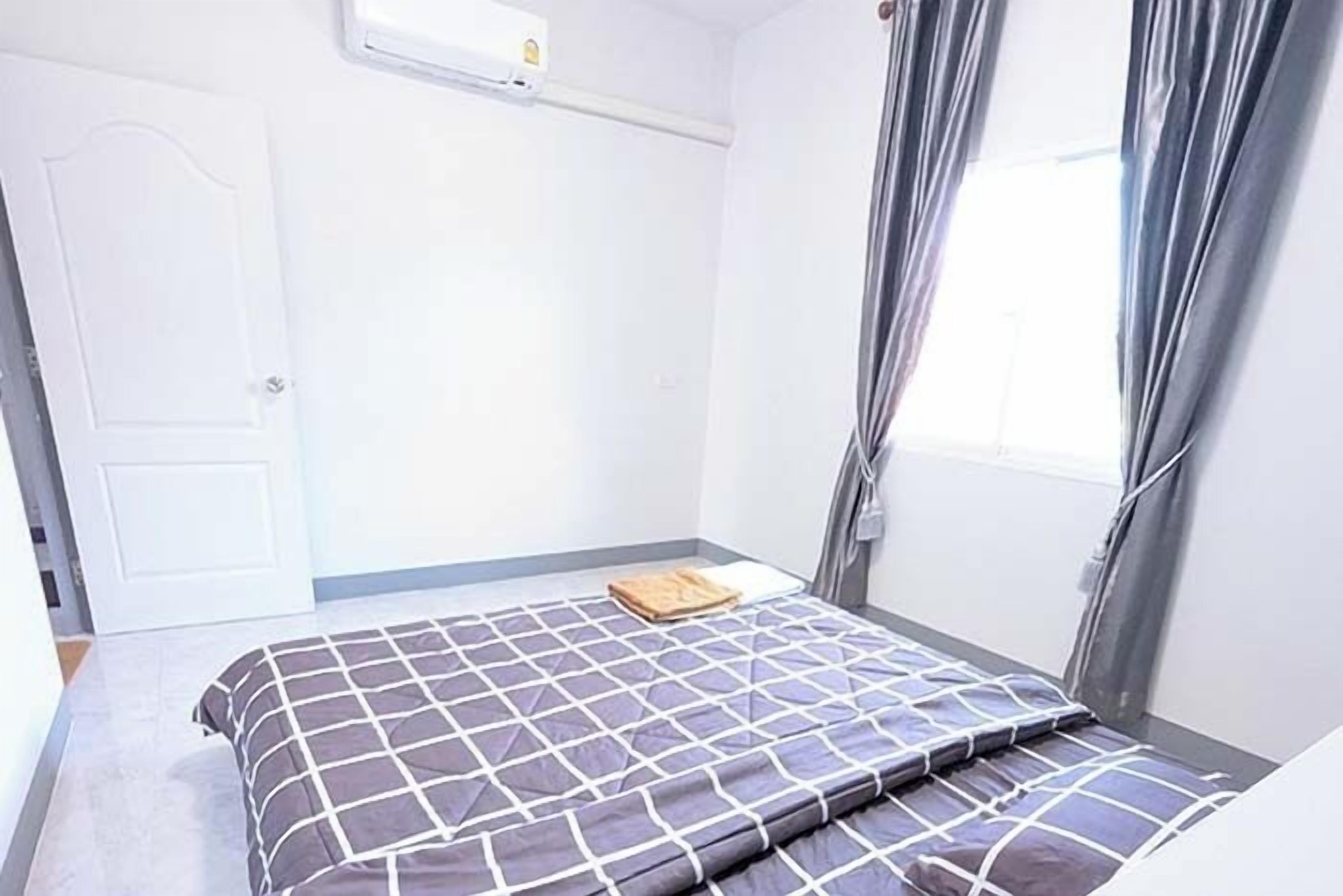 A small, clean room with a bed, a door, and a window with curtains.