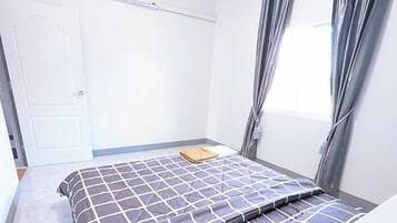 A small, clean room with a bed, a door, and a window with curtains.