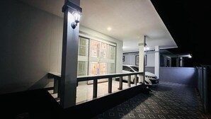 Un espacio al aire libre cubierto con piso estampado, un coche blanco estacionado adentro, y un edificio con un amplio ventanal y una puerta.
