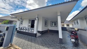 Una casa de dos pisos con un porche cubierto, un camino de entrada empavedado y una motocicleta estacionada.