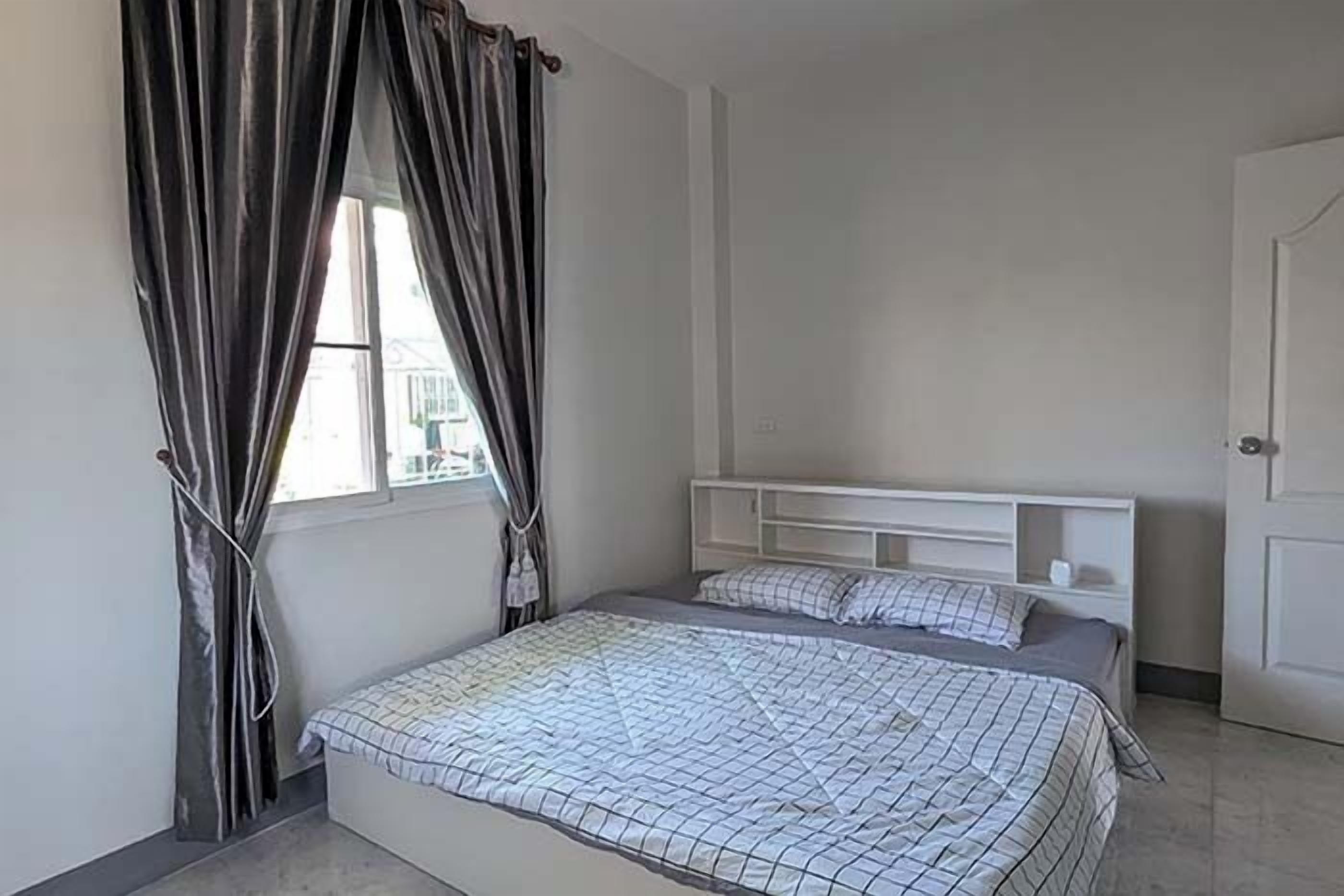 A bedroom with a bed, a window with curtains, a white headboard, and a door.