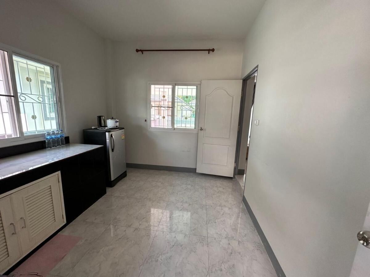 A kitchen with a refrigerator, a water dispenser, and a window with metal bars.