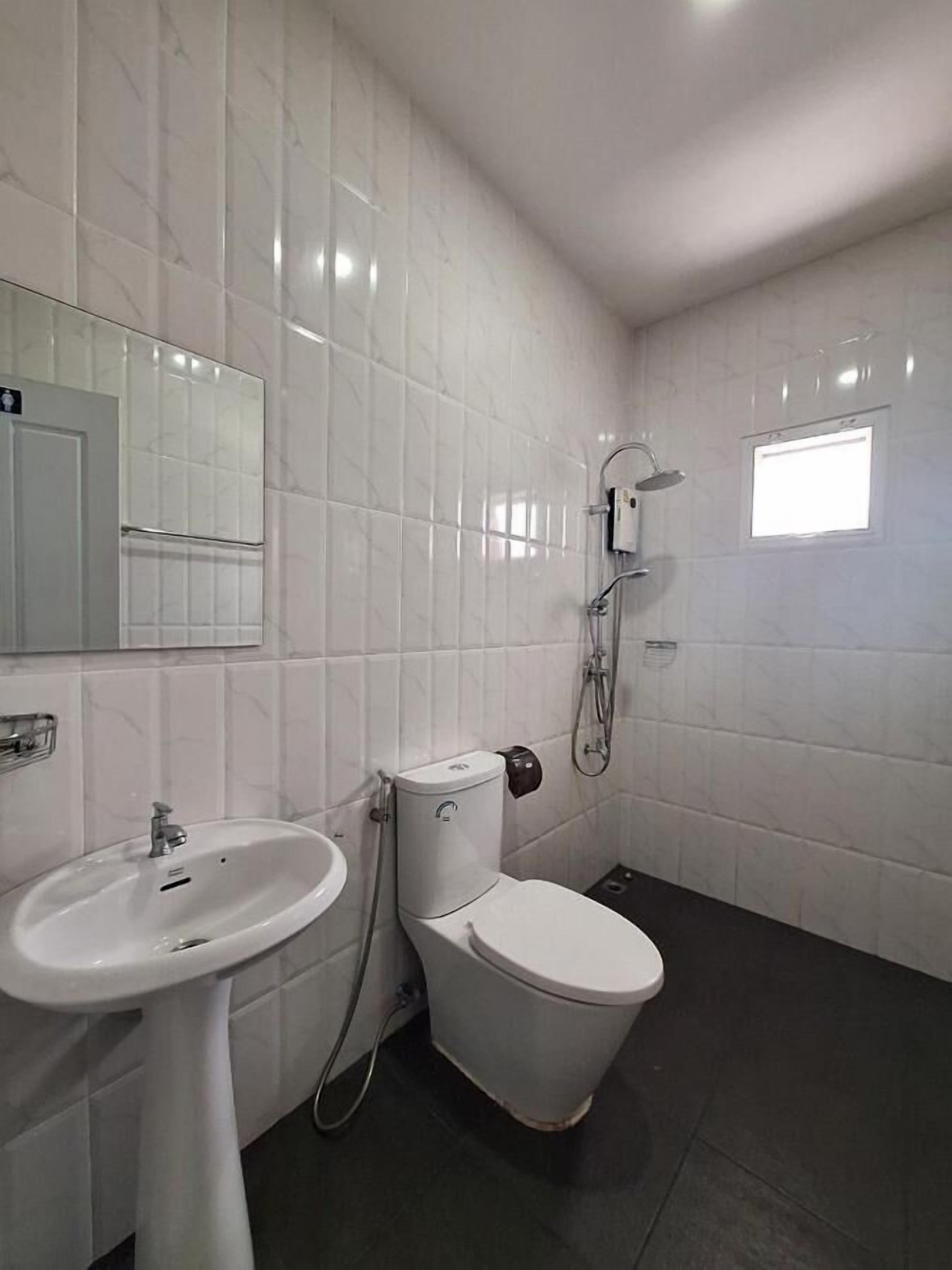 Un baño con paredes de azulejos blancos, un lavamanos blanco, un inodoro y una ducha.
