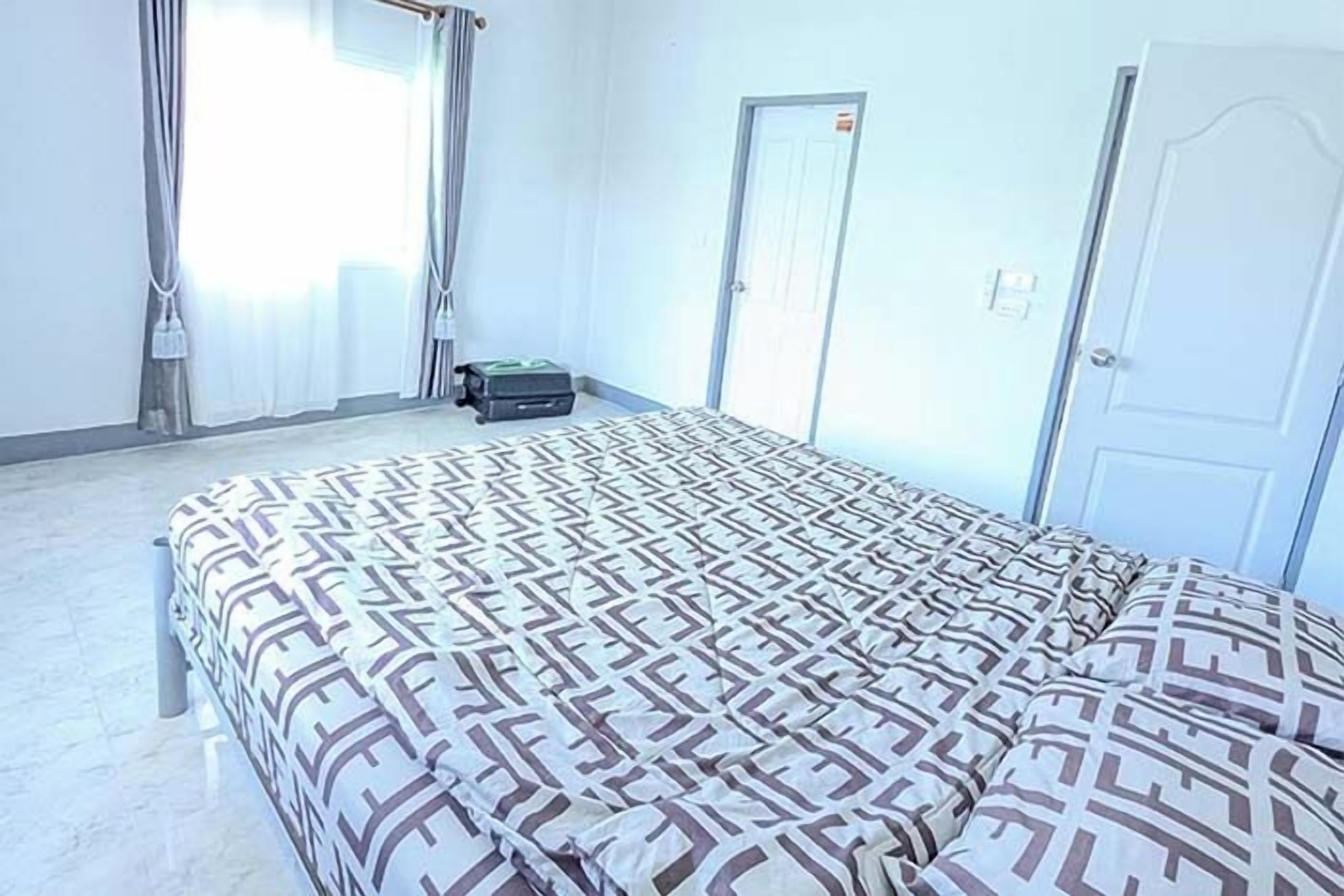 Quarto de hotel com cama, cortinas, porta e mala no chão.
