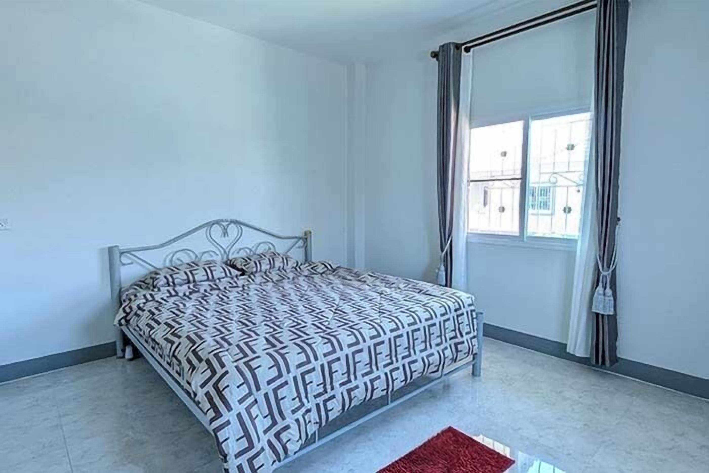 A bedroom with a patterned bedspread, a red rug, and a window with curtains.