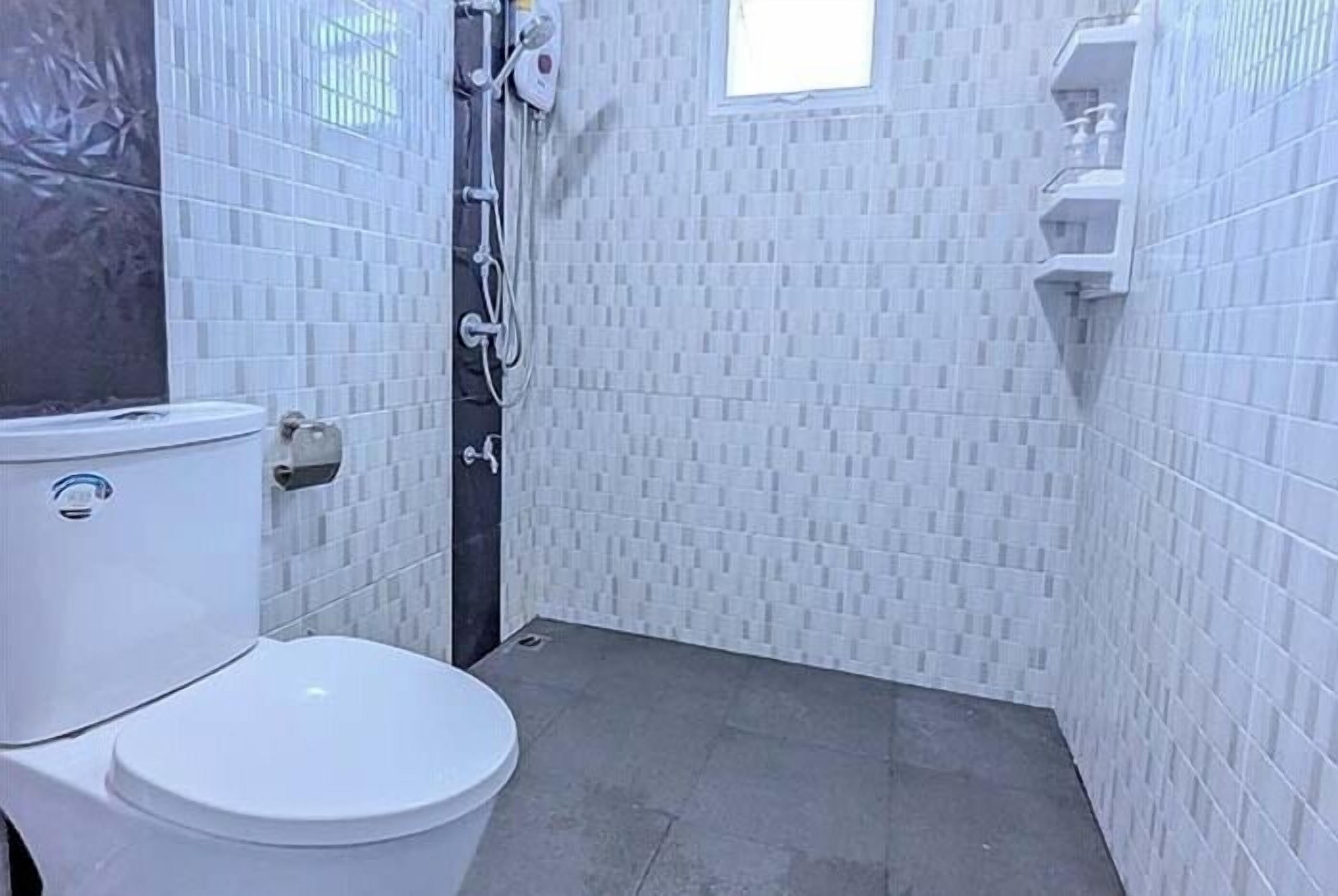 A small, tiled bathroom with a toilet, a shower, and a window.