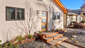 Ein modernes Haus mit heller Fassade, einer Holztür und einer kleinen Veranda mit Stufen.