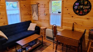 Ein gemütliches Blockhauss-Interieur mit einem dunkelblauen Sofa, einem Holzespeisesaal mit Stühlen und einem kleinen Hocker.
