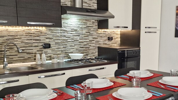 A modern kitchen with a stone backsplash, a gas stove, and a dining area set for four with red placemats and white plates.