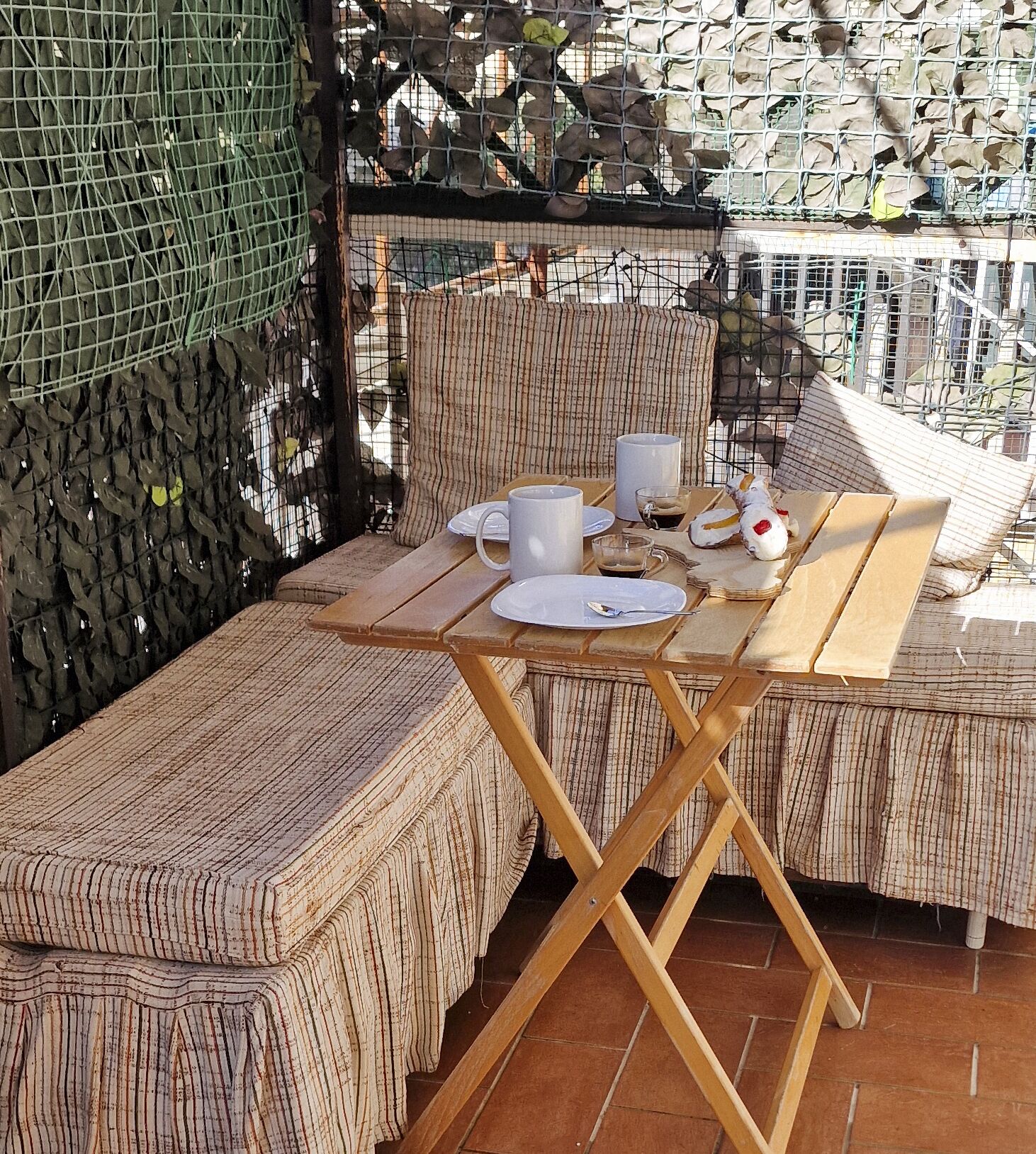 Une table en bois, dressée avec des assiettes, des tasses et une cuillère, entourée de coussins à rayures.