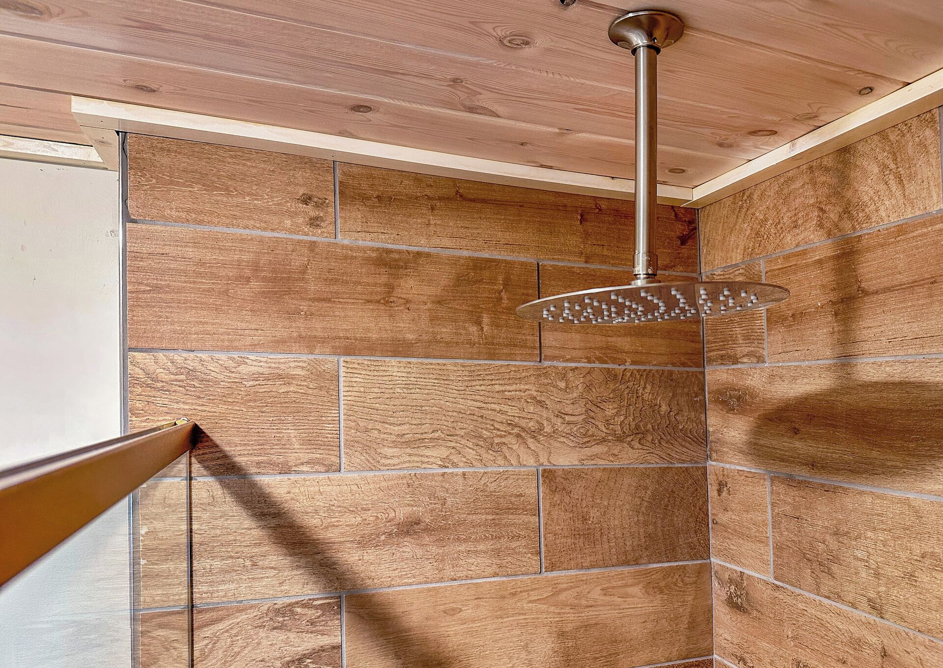 Une douche dotée d’un pommeau de douche à effet pluie, de carreaux muraux en bois et d’une poutre apparente au plafond.