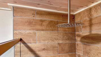 Una ducha con cabezal de ducha tipo lluvia, azulejos de madera y una viga de techo visible.