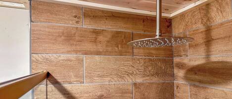 Une douche dotée d’un pommeau de douche à effet pluie, de carreaux muraux en bois et d’une poutre apparente au plafond.