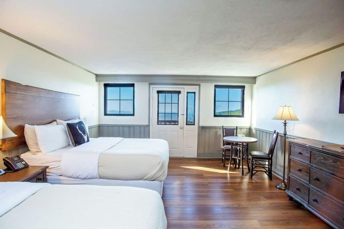 A hotel room with two beds, a dining area, and a view of the outdoors.