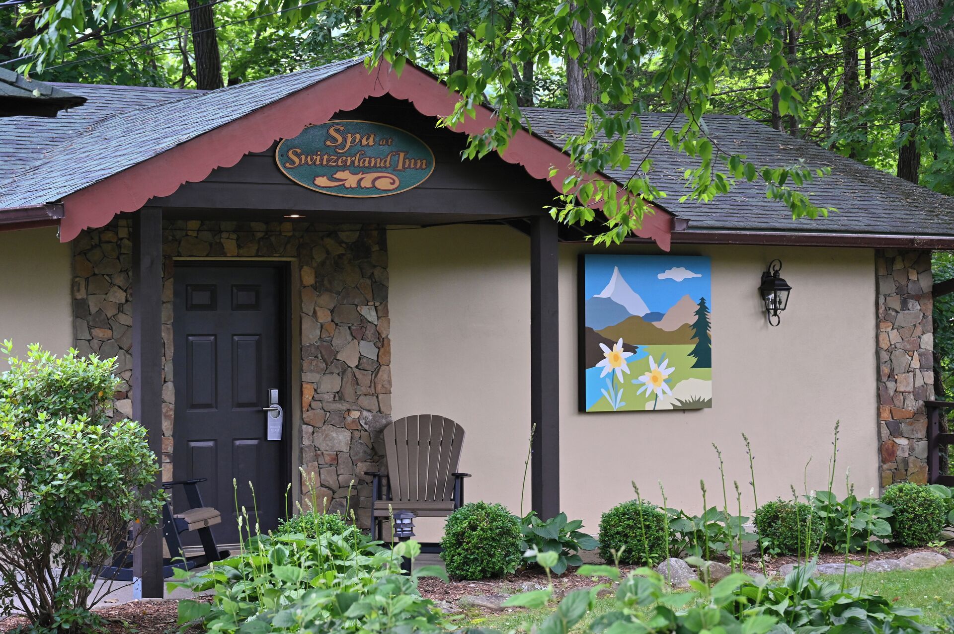 A spa named 'Spa at Switzerland Inn' with a stone facade, a black door, a bench, and a painting of a mountain landscape.