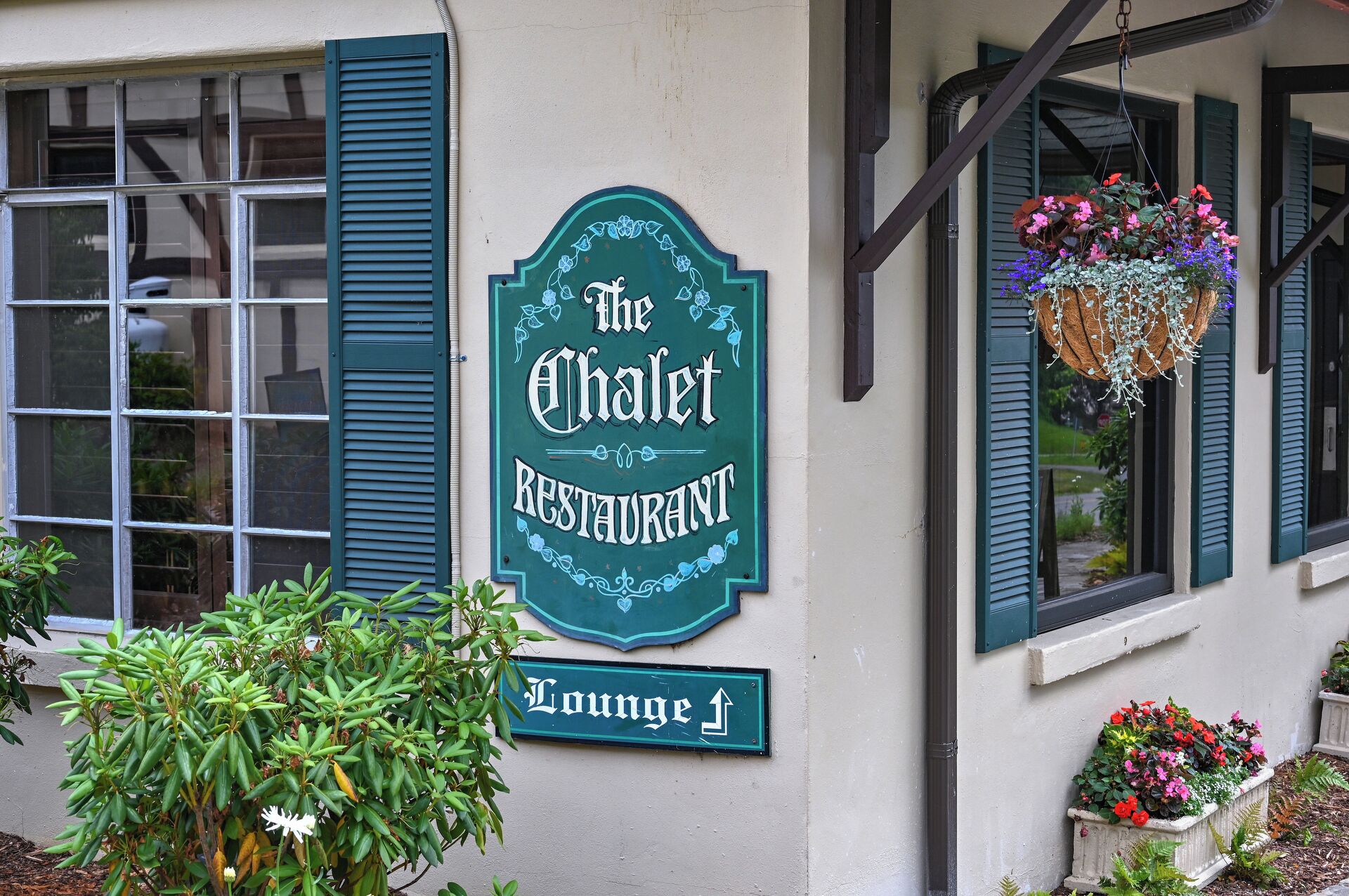 A restaurant sign with a green border and a hanging flower basket.