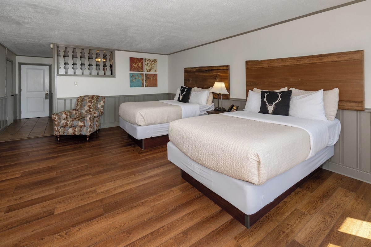 A hotel room with two beds, a chair, and a wooden floor.