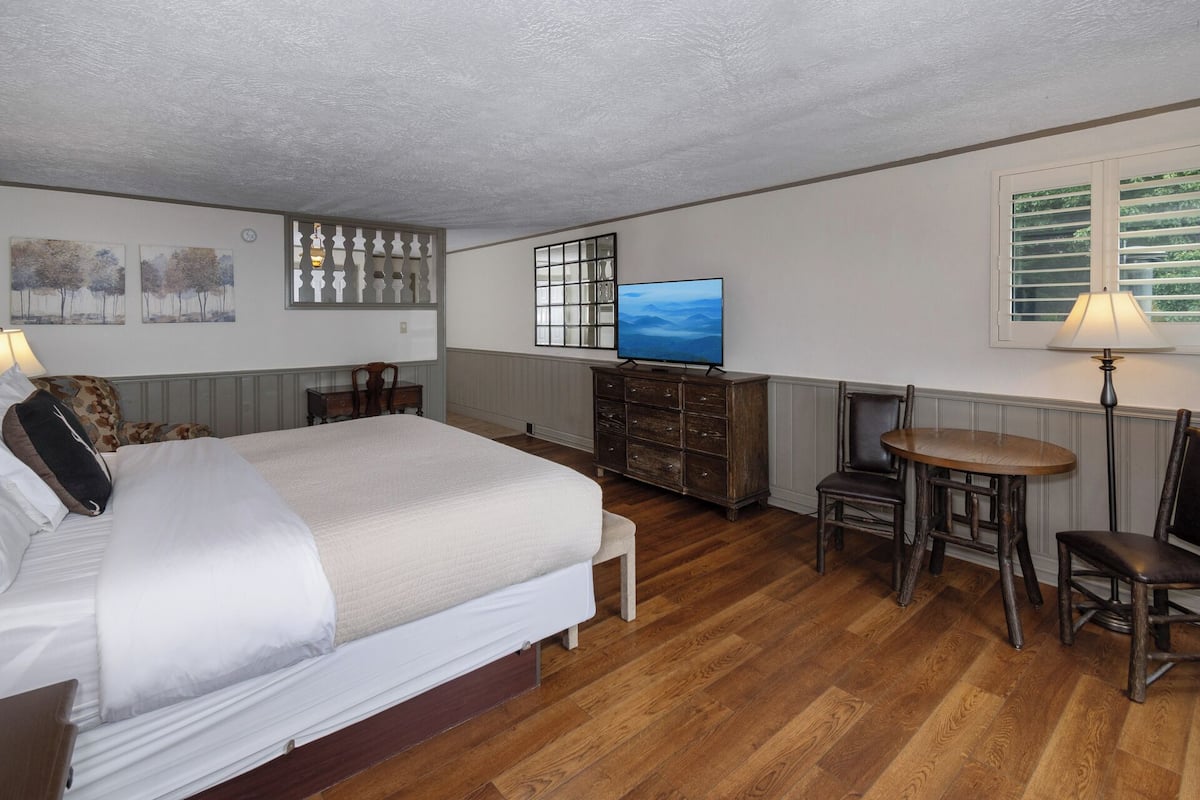 A bedroom with a bed, a dresser, a television, a chair, and a table.