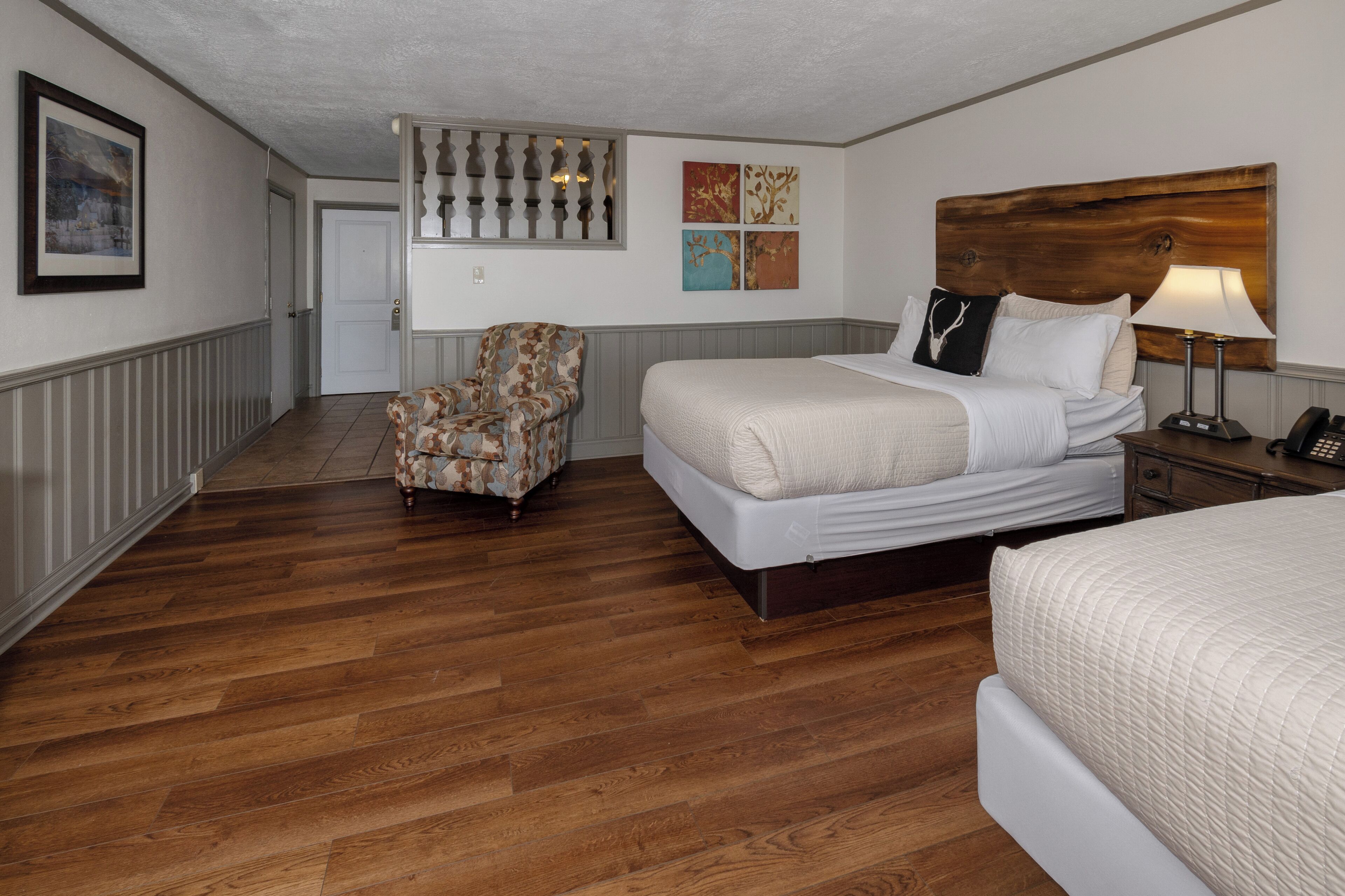A hotel room with a large bed, a chair, a nightstand, and a wall with artwork.